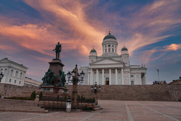 Helsinki Cathedral's neoclassical architecture is set against a vibrant sunset sky. The statue of...