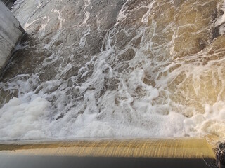 part of concrete old dam on river with flow of water and white foam on summer street