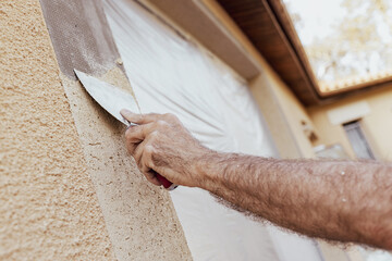 Worker’s hand plastering exterior walls of a house with a spatula. Renovation of a building...