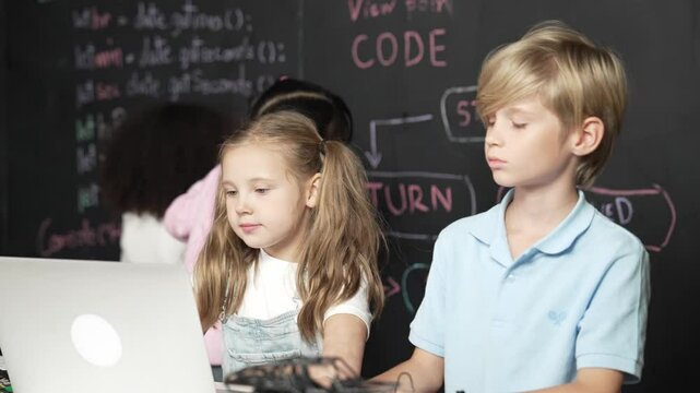 Smart girl using laptop programing engineering code with diverse friends ay table with microchip and main board scatter around in STEM classroom at blackboard written with coding prompt. Erudition.