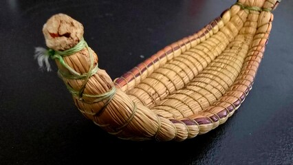A close-up of a small, intricately woven boat made from natural fibers, with green thread binding...