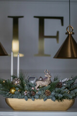 Christmas table composition made of fresh nobilis spruce, white candles, pine branches with glass balls and decorative gold deer. Happy New Year decorations.