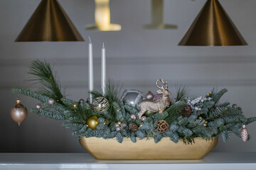 Christmas table composition made of fresh nobilis spruce, white candles, pine branches with glass balls and decorative gold deer. Happy New Year decorations.