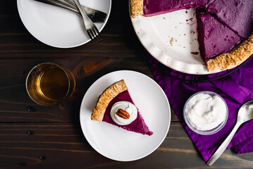 Slice of Purple Sweet Potato Pie Topped with Whipped Cream and a Pecan: Side view of a homemade purple sweet potato pie with a glass of bourbon