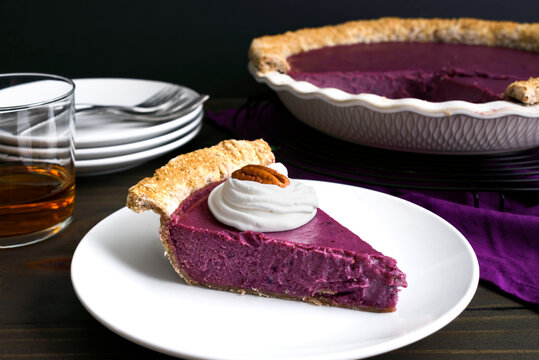 Slice of Purple Sweet Potato Pie Topped with Whipped Cream and a Pecan: Side view of a homemade purple sweet potato pie with a glass of bourbon