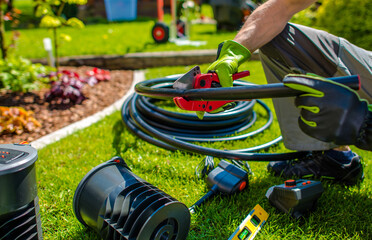Gardener Preparing Tools and Irrigation System Hose for Landscaping Task in a Sunny Backyard Setting
