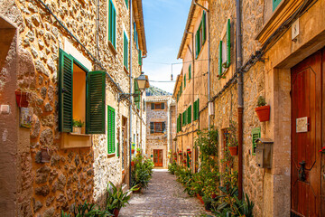 Stone paved narrow street, plants in ceramic pots, stone built houses, wooden green windows, in Valdemossa medieval village, Mallorca, Balearic Islands, Spain