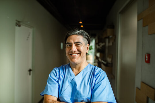 Smiling healthcare professional portrait in scrubs with arms crossed in hallway