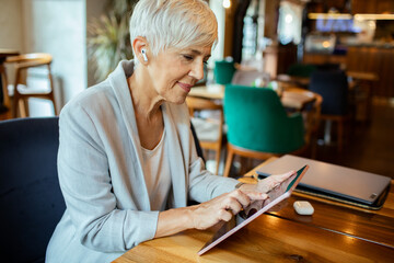 Senior woman using tablet with earbuds in a cozy cafe setting