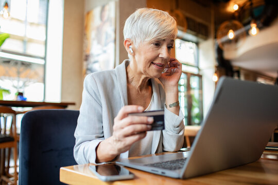 Senior businesswoman using credit card on laptop in cafe
