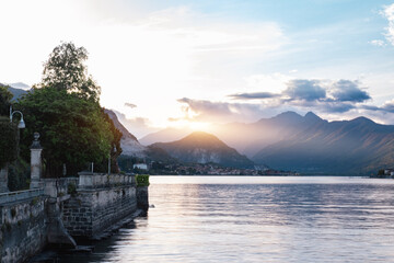 Scenic View Of Lake Como At Sunset, With Golden Light Illuminating The Mountains And A Promenade In...