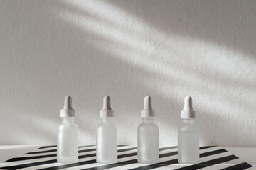 Four Frosted Glass Dropper Bottles Stand On A Striped Surface, Showcasing Skincare Or Essential Oil Products, Illuminated By Natural Light