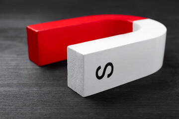 One horseshoe magnet on black wooden table, closeup