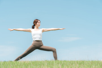 青空の下でヨガ・ピラティス・ストレッチをする若いアジア人女性

