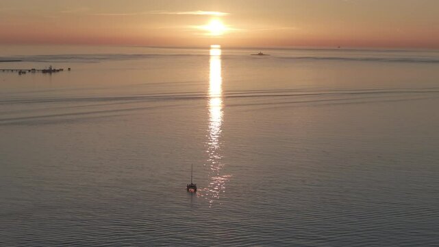 Aerial drone shot of the Tagus river, Atlantic Ocean and horizon at sunset in Lisbon, Portugal, Europe. Catamaran facing the sun. Forte do Bugio lighthouse visible. Shot in ProRes 422 HQ