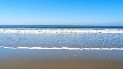 Fototapeta premium A tranquil seascape with a blue sky, calm waves, and a sandy beach.