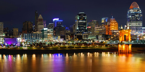 Obraz premium Cincinnati City Skyline Nightscape over the Ohio River with Roebling Suspension Bridge with light reflections on the water in Kentucky, USA