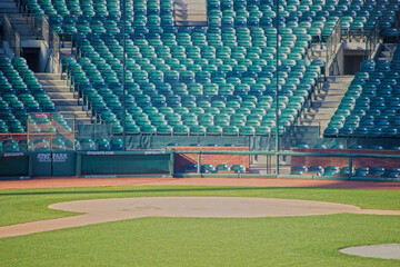 Empty baseball stadium with rows of green seats surrounding the field. The focus is on the home plate area of the baseball diamond, with the pitcher's mound and the infield grass clearly visible.