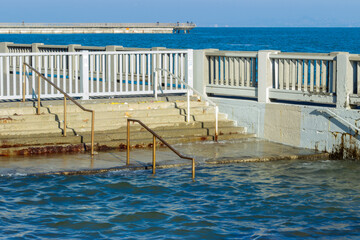 Steps and a railing near the Embarcadero in San Francisco submerged in water during a king tide, this scene highlights the impact of rising sea levels and coastal flooding on urban infrastructure.