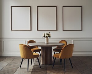 An elegant dining area. A round wooden table with a unique cylindrical base is surrounded by four mustard-colored velvet chairs.  3 large blank square frames is hung on a white wall.