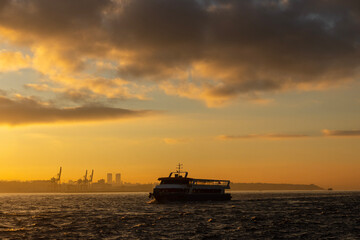 Fototapeta premium A sunrise over the Bosphorus Strait with a large ferry boat that sails across the water. The city skyline of Istanbul is visible in the distance, adding a touch of urban life to the scene.
