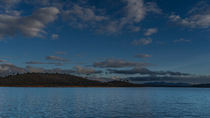 Fototapeta premium A calm blue lake. Ripples on the surface of the water. Coastal hills against the background of the evening sky and clouds. Madagascar. Mantasoa Lake