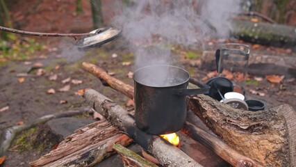 Caucasian Male Hiker Tourist Heating Water in Metal Pot Over Paraffin Wax Heater and Improvised Campfire at Bushcraft Forest Camping Spot