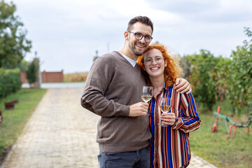 Young couple with glass of vine in hands hug and smile in vineyard