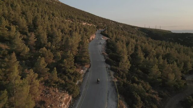 Motorbike in the pine forest on the mountain, aerial footage on sunset 