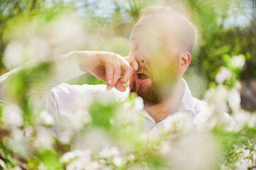 Man allergic suffering from seasonal allergy at spring in blossoming garden at springtime. Close up...