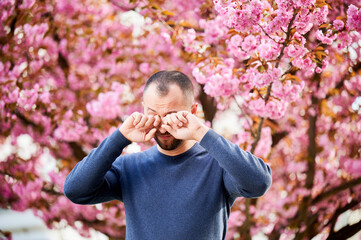 Man allergic suffering from seasonal allergy at spring in blossoming garden at springtime. Bearded...