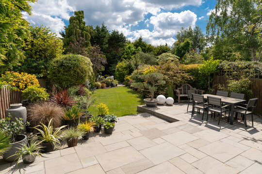 Beautiful English garden in summer with Indian sandstone patio and attractive shrubs, seating and blue sky.