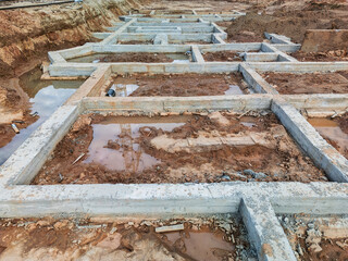 Construction site foundations forming geometric patterns in wet earth under a cloudy sky