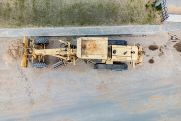 Aerial view of a heavy grader parked on a dusty road near a construction site in the afternoon sun...