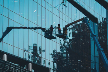 Male window cleaner cleaning glass windows on modern building high in the air on a lift platform....