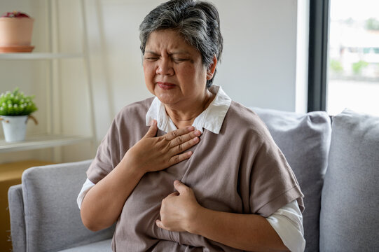 An elderly Asian woman experiencing acid reflux, chest tightness, bloating, and throat burning due to gastrointestinal issues.Senior health or health care concept 