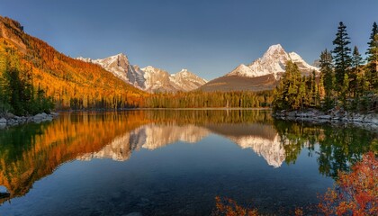 Naklejka premium Crystal-Clear Lake at the Base of Towering Snow-Capped Mountains, Reflecting the Majestic Peaks and Vibrant Colors of the Surrounding Trees in the Early Morning Light