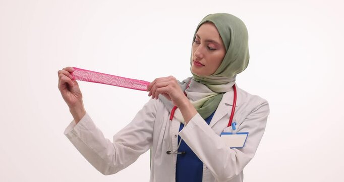 Serious female Muslim doctor demonstrates flexibility of condom at college. Woman in hijab with stethoscope conducts sex lesson for teenage students slow motion