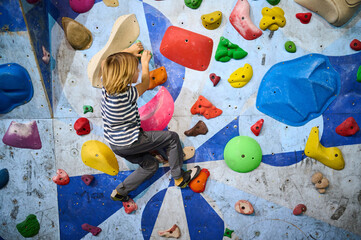 A 6-year-old boy climbing on a vibrant indoor bouldering wall with multicolored holds, engaging in...