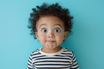 Naklejka premium A cute child with curly hair and a surprised expression poses against a bright blue background, showcasing innocence and playfulness, looking at the camera