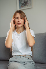 Young woman experiencing headache while sitting on a couch in a modern living room home during daytime vertical photo