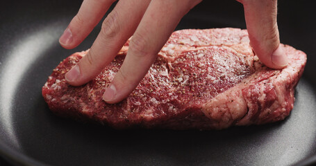Closeup shot of man hands put ribeye steak on non stick pan