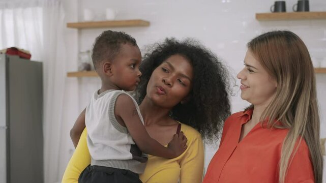 Family of happy interracial lesbian couple and black cute son hugging and kissing with emotional love and happiness moment in kitchen room at home. Female black and white LGBTQ pride with boy child. 