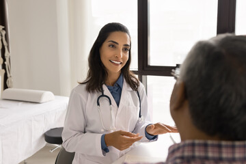Fototapeta premium Young 30s Latin woman medical practitioner or cardiologist gives professional advices, health recommendations to older male patient at his visit at hospital. Treatment plan, chronic disease prevention