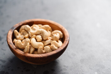 Dry cashew nuts in wood olive bowl on concrete background with copy space