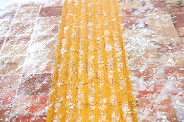 Snowy sidewalk with yellow tactile paving slabs, closeup. Difficult conditions for walking visually...
