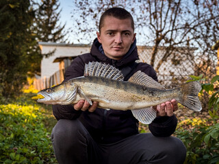 Man holds chub fish out in front of him in a boat. Portrait of smiling bearded man fishing catching fish at remote lakeside. Zander fish.