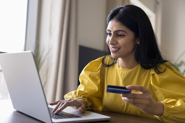 Happy young Indian customer woman paying for online purchase by credit card, using Internet bank...