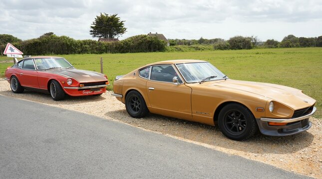 A pair of Classic Datsun Z Sports cars. A Red 1973 240Z, and a yellow 1978 260Z.  Utah Beach, France, July 2023. 