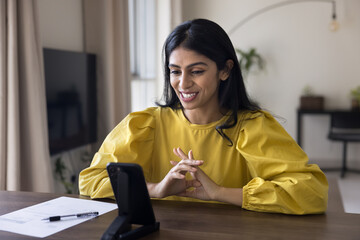 Positive young Indian freelance worker girl speaking at cellphone web camera, talking on video...